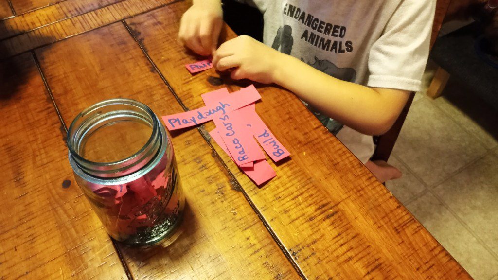Child folding pink paper and putting them in the mason jar