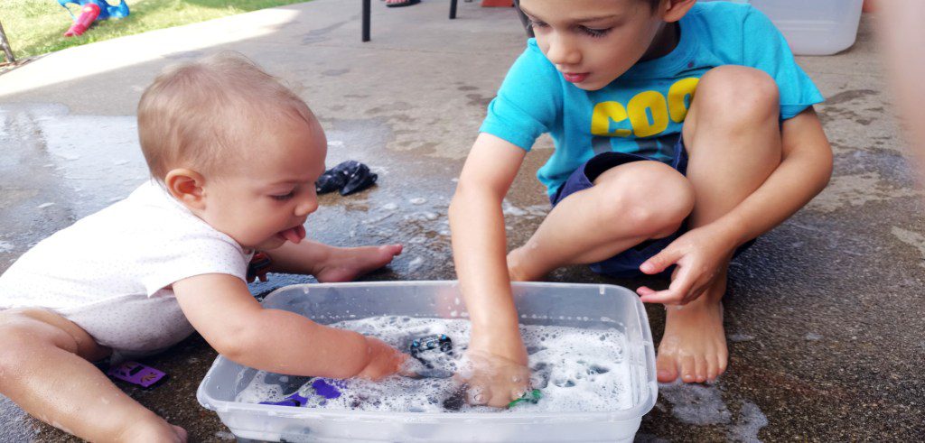 2 kids playing with soapy water and toy cars