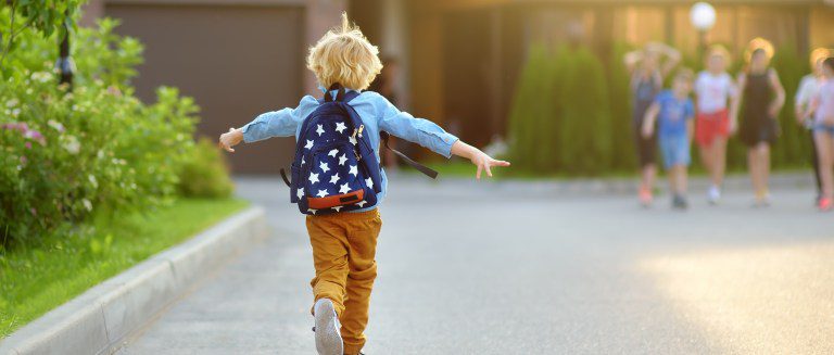 Kid wearing backpack happily walking on a sidewalk