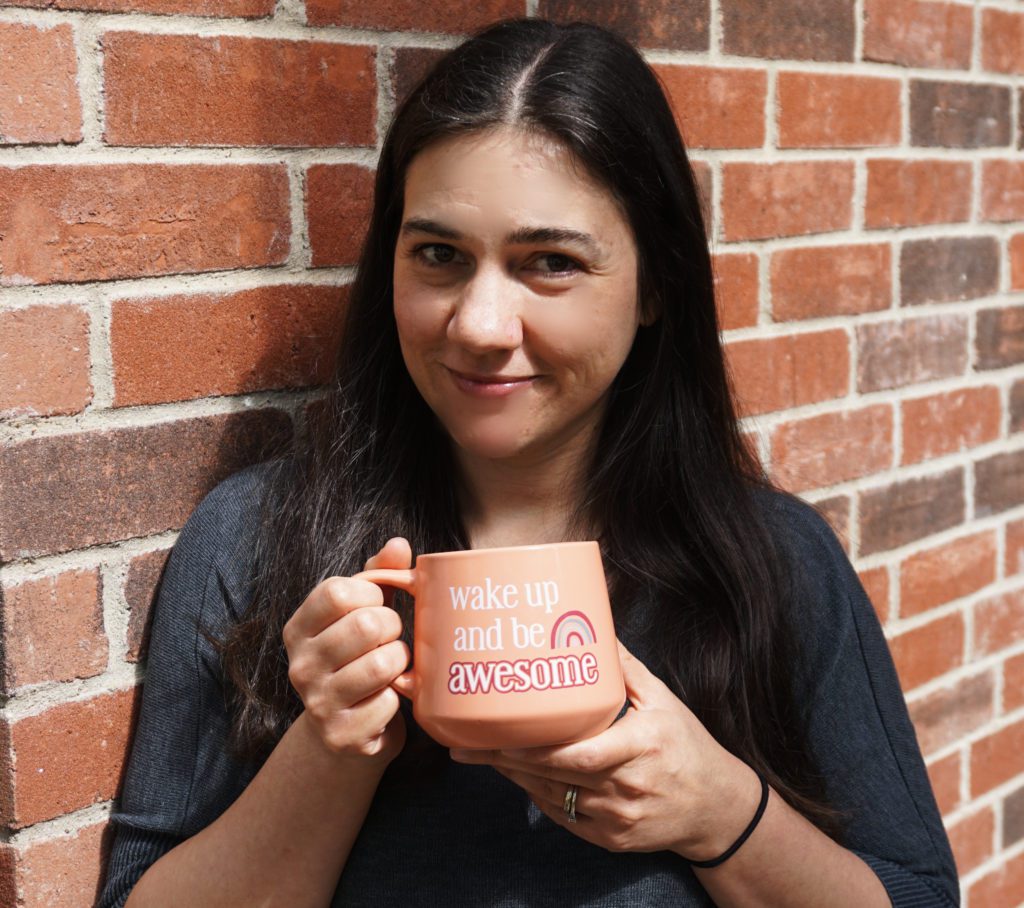 Sarah holding a cup while posing on a brick wall